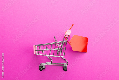 Composition of shopping cart and gift tag on pink background