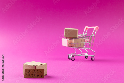 Composition of shopping cart with boxes and black friday text on pink background