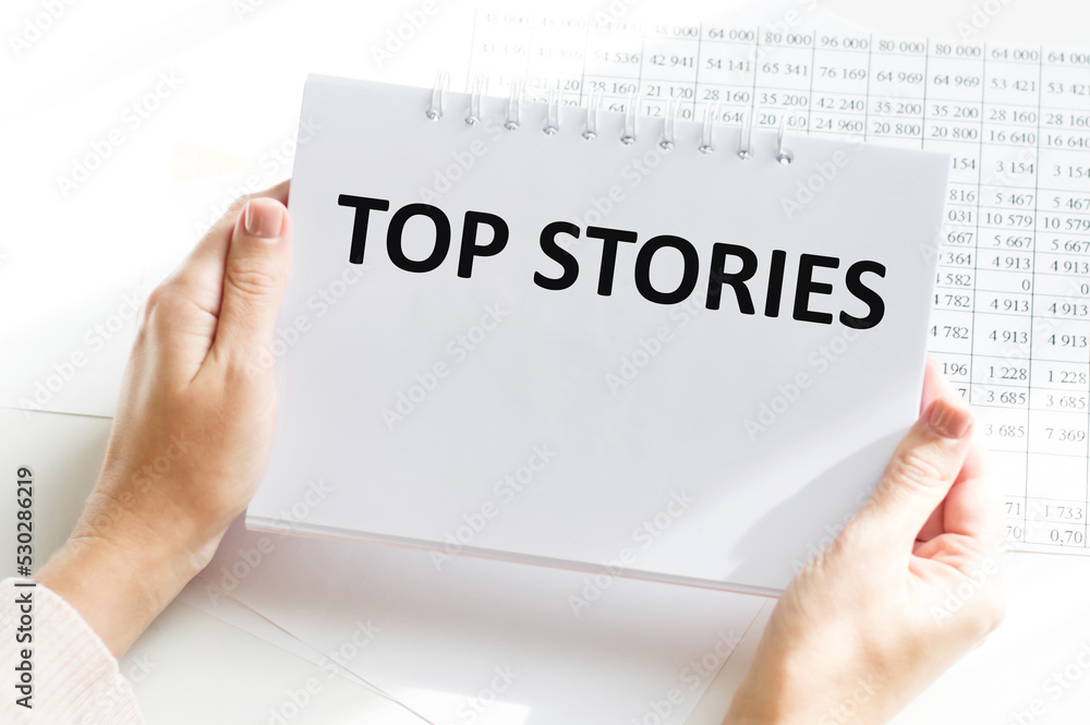 Word TOP STORIES on a notebook on a table in the hands of a person Word TOP STORIES on a notebook on a table in the hands of a person
