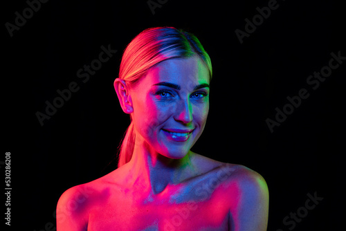 Young beautiful woman with well-kept skin and stylish makeup isolated over dark background in pink neon light. Concept of beauty, art, fashion