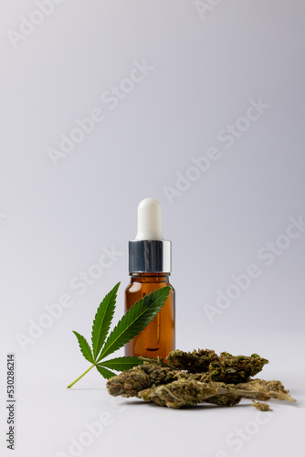 Vertical image of bottle of cbd oil and marihuana leaf on white surface