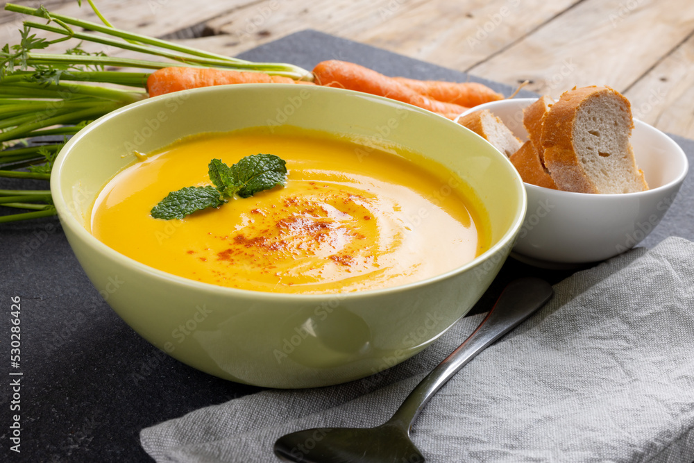Horizontal image of bowl of carrot soup with garnish, raw carrots and sliced bread on slate Horizontal image of bowl of carrot soup with garnish, raw carrots and sliced bread on slate
