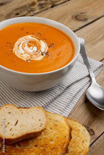 Vertical image of bowl of tomato soup with spoon and toast on wooden table