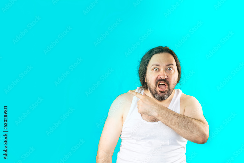 A joyful unshaven man in a white undershirt, smiling, points aside with his finger. Unemployed slovenly dressed man from Eastern Europe. A joyful unshaven man in a white undershirt, smiling, points aside with his finger. Unemployed slovenly dressed man from Eastern Europe.