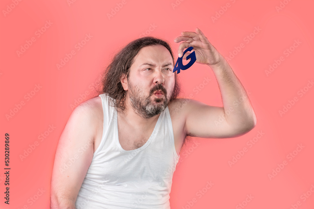 A surprised unshaven man in a white undershirt looks at the 4G sign with disgust and disdain. An unemployed, unkemptly dressed adult from Eastern Europe. A surprised unshaven man in a white undershirt looks at the 4G sign with disgust and disdain. An unemployed, unkemptly dressed adult from Eastern Europe.