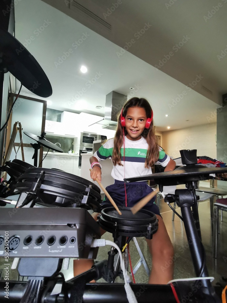 Obraz premium Happy girl with headphones playing a percussion instrument such as the drums. Solfeggio and music lessons