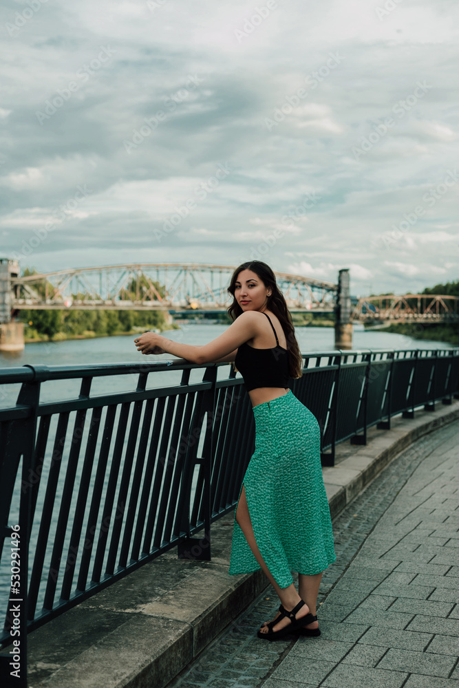 Portrait of a beautiful young brunette on the bridge by the river