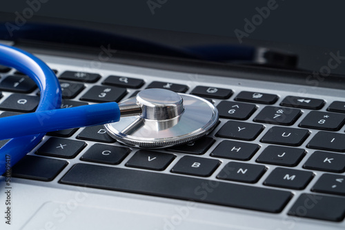 Blue stethoscope on laptop computer keyboard, medical design concept.