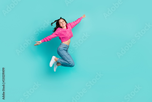 Full length photo of gorgeous adorable woman dressed pink sweater jeans sneakers flying arms plan wings isolated on teal color background