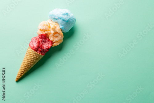 Horizontal image of three coloured flavours of ice cream in cone, on blue background with copy space