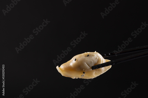 Overhead view of asian dumpling held in black chopsticks on black background
