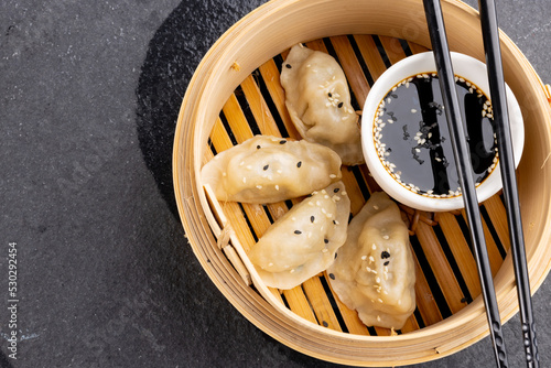 Overhead view of asian dumplings, soy sauce and chopsticks in wooden dish on grey background