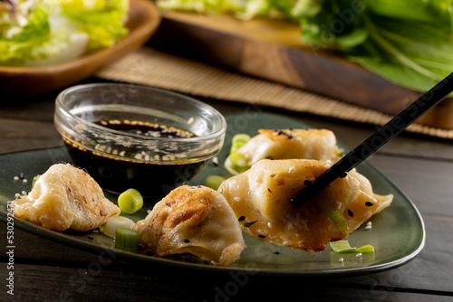 Close up of asian dumplings, soy sauce and chopsticks with plate and wooden background