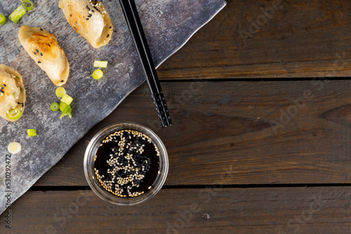 Overhead view of asian dumplings, soy sauce and chopsticks with slate and wooden background
