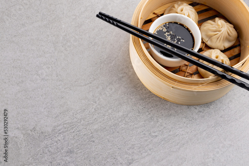 Overhead view of asian dumplings, soy sauce and chopsticks in wooden dish with copy space on grey
