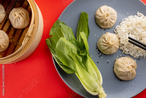 Overhead view of asian dumplings, rice, endive and chopsticks on red background