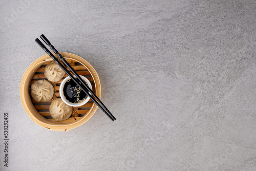 Overhead view of asian dumplings, soy sauce and chopsticks in wooden dish with copy space on grey