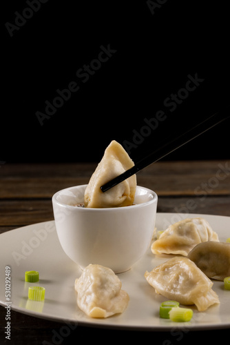 Close up of asian dumplings, soy sauce and chopsticks on plate and wooden background