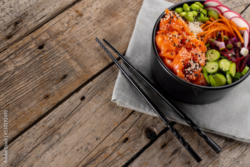 Overhead view of hawaiian poke bowl with chopsticks and copy space on wooden background