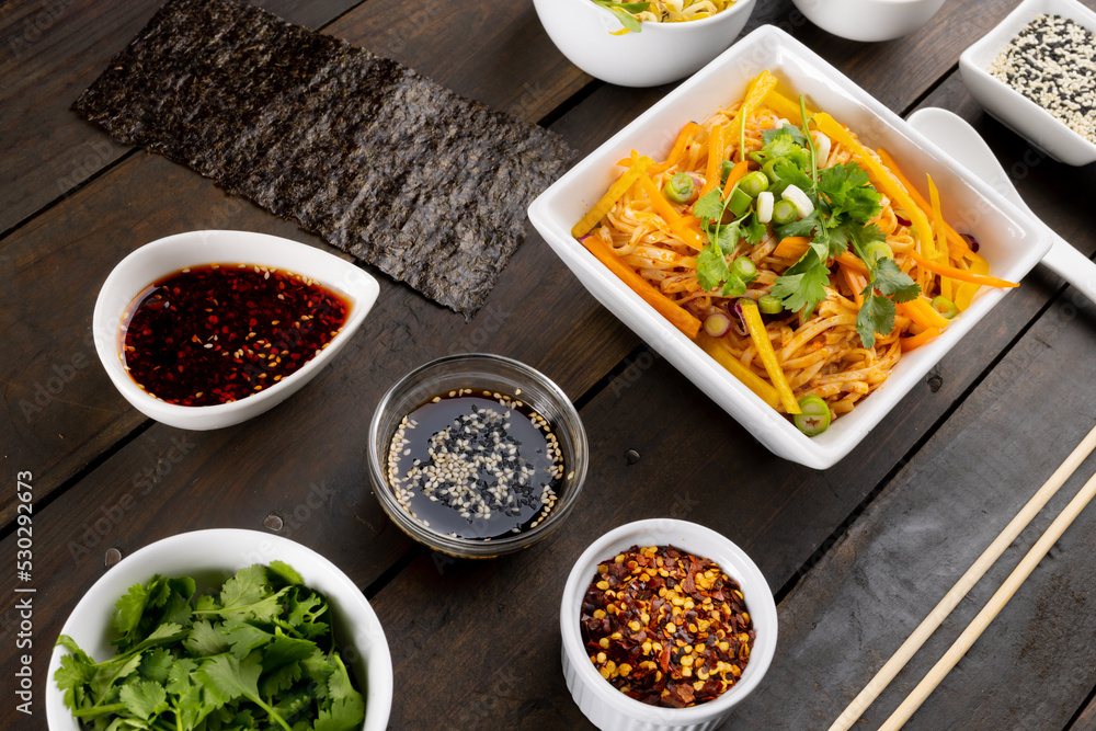 Overhead view of asian wok stir fry noodles with chopsticks and condiments on wood Overhead view of asian wok stir fry noodles with chopsticks and condiments on wood