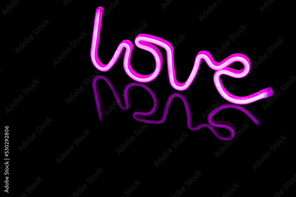 Image of vibrant neon love text formed with pink glow sticks over black background and copy space