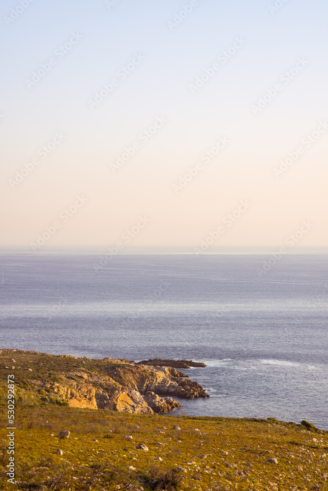 Landscape of calm sea and sea shore with rocks, blue cloudless sky and horizon
