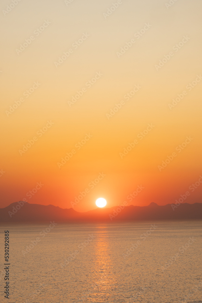 Landscape of sea, sea shore with mountains, sun on cloudless sky at sunset and horizon