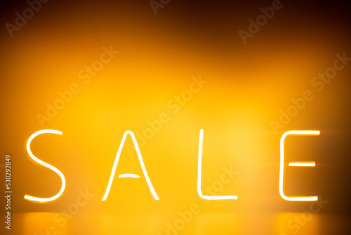 Image of glowing neon sale text over orange background