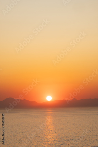 Landscape of sea  sea shore with mountains  sun on cloudless sky at sunset and horizon