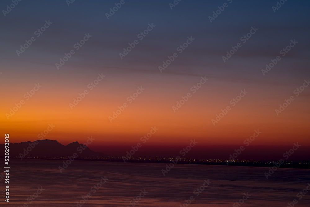 Landscape of sea, sea shore with mountains, cloudless sky at sunset and horizon