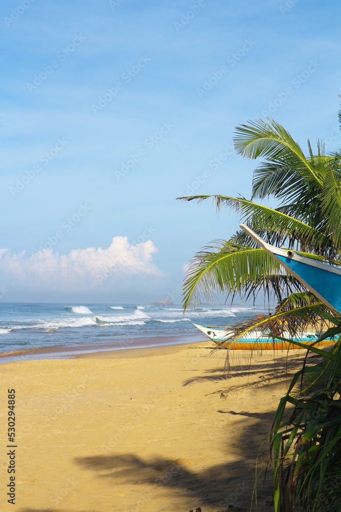 Paradise beach with yellow sand, palm trees and a boat in Sri Lanka, Hikkaduwa.