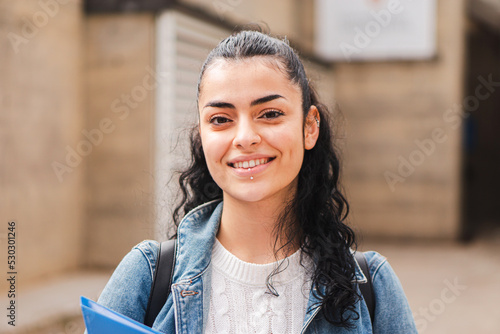 Pretty hispanic female student smiling and looking at camera in the high school. Head shot portrait of latin teenager girl standing outdoors at the university campus. Education concept. High quality
