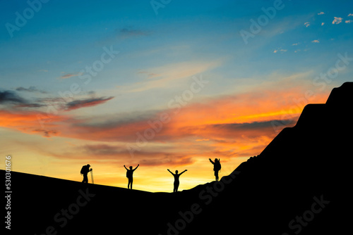 Silhouette of small group young traveler standing open arms on top of the mountain in the morning. They was delighted and happy to come and see the sunrise from the top of the mountain.