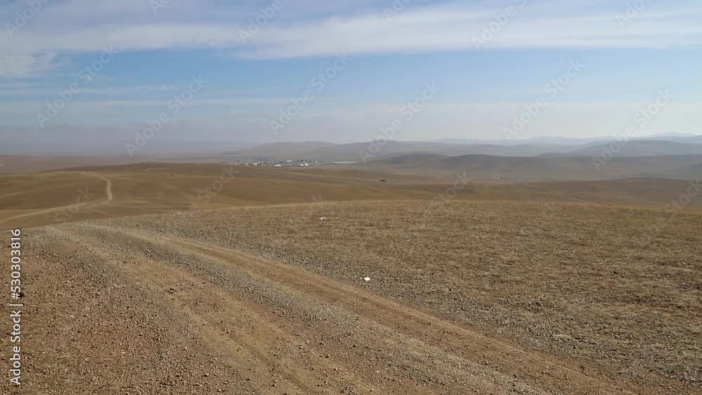 Vast hilly landscape in the Mongolian steppe. Pan view footage over the horizon over land. Unpaved road through the endless vast steppe of central Mongolia. Far horizon over land. Adventure travel Vast hilly landscape in the Mongolian steppe. Pan view footage over the horizon over land. Unpaved road through the endless vast steppe of central Mongolia. Far horizon over land. Adventure travel