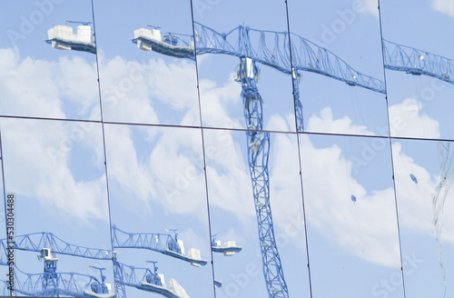 Blue construction cranes reflected in panes of shiny glass