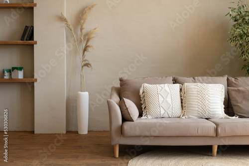Sofa with macrame cushions on a woven round rug in a modern living room in beige tones. Cozy interior of a country house. photo