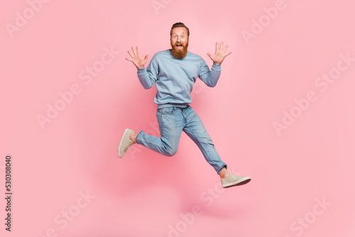 Full length photo of carefree astonished man jumping run raise opened hands isolated on pink color background