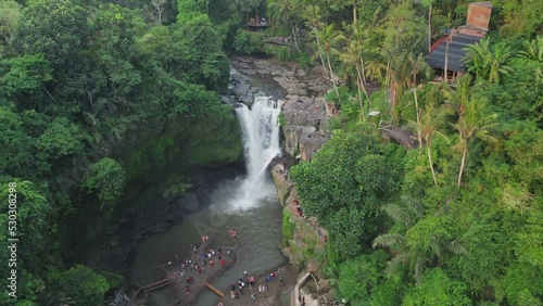 Flying over the tourist waterfall tegenungan where a large crowd of vacationers and tourists swim. Tourist attractions of Bali taken from a drone. Tourist season with a lot of people photo