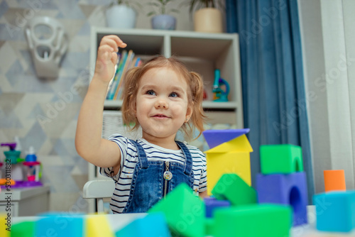 The little girl plays with colorful toy blocks and builds a tower. Educational and creative toys and games for young children.