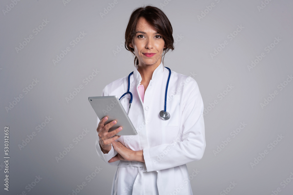 Smiling female doctor with digital tablet standing at isolated grey background Smiling female doctor with digital tablet standing at isolated grey background