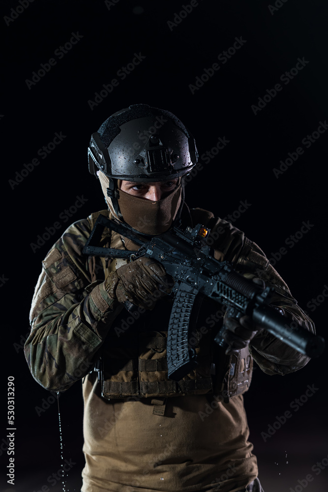 Army soldier in Combat Uniforms with an assault rifle, plate carrier and combat helmet going on a dangerous mission on a rainy night. 