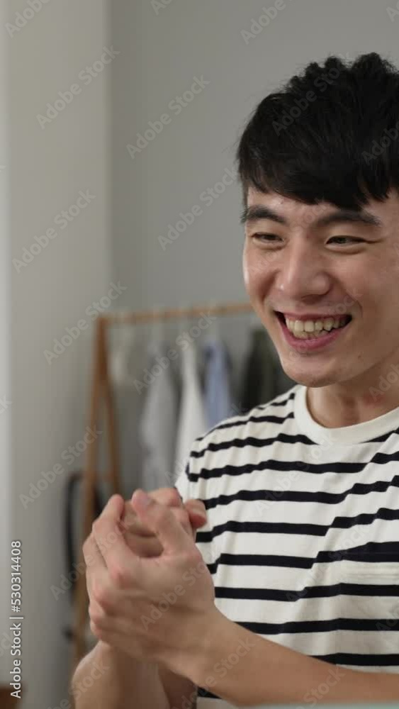 Vertical Screen: slow motion of overjoyed asian young man is leaning near computer screen to check in excitement while cheering for getting job offer online with strong hand gesture at home. Vertical Screen: slow motion of overjoyed asian young man is leaning near computer screen to check in excitement while cheering for getting job offer online with strong hand gesture at home.