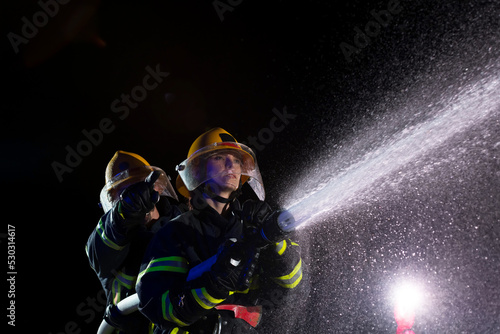 Fototapeta Naklejka Na Ścianę i Meble -  Firefighters using a water hose to eliminate a fire hazard. Team of female and male firemen in dangerous rescue mission. 