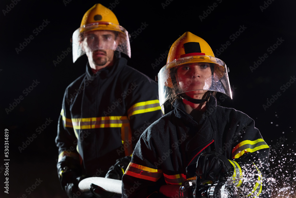 Firefighters using a water hose to eliminate a fire hazard. Team of female and male firemen in dangerous rescue mission. Firefighters using a water hose to eliminate a fire hazard. Team of female and male firemen in dangerous rescue mission.