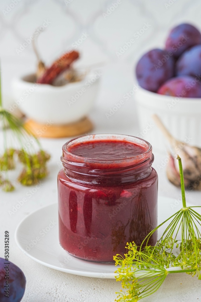 Tkemali, spicy plum sauce in a glass jar on a light concrete background. Fruit sauces, preservation, preparations. Tkemali, spicy plum sauce in a glass jar on a light concrete background. Fruit sauces, preservation, preparations.