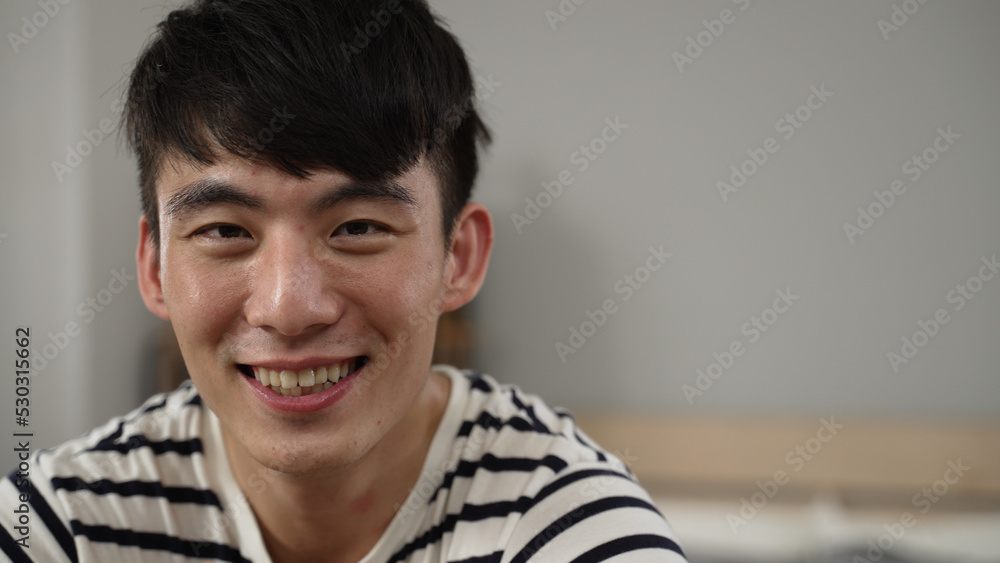 closeup with front view of a distracted asian college boy learning from home is propping face and chuckling at the camera while daydreaming in the bedroom closeup with front view of a distracted asian college boy learning from home is propping face and chuckling at the camera while daydreaming in the bedroom
