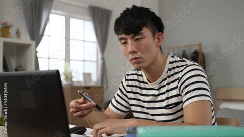 closeup asian Korean university boy holding face with boredom is looking away into empty area and spinning pen while learning from home watching online video lecture.