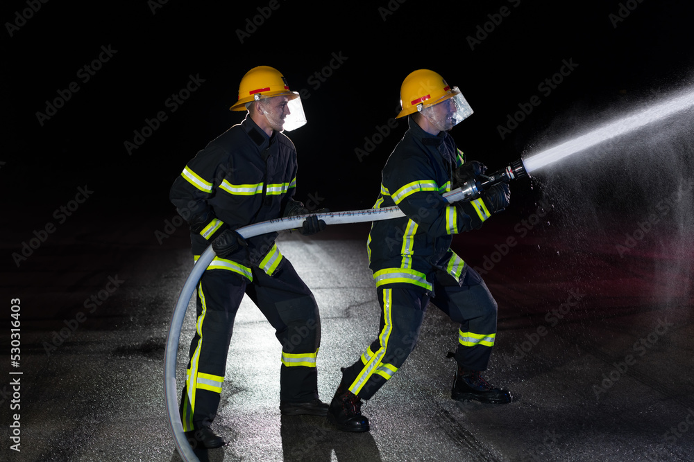Firefighters use a water hose to eliminate a fire hazard. Team of firemen in the dangerous rescue mission. Firefighters use a water hose to eliminate a fire hazard. Team of firemen in the dangerous rescue mission.