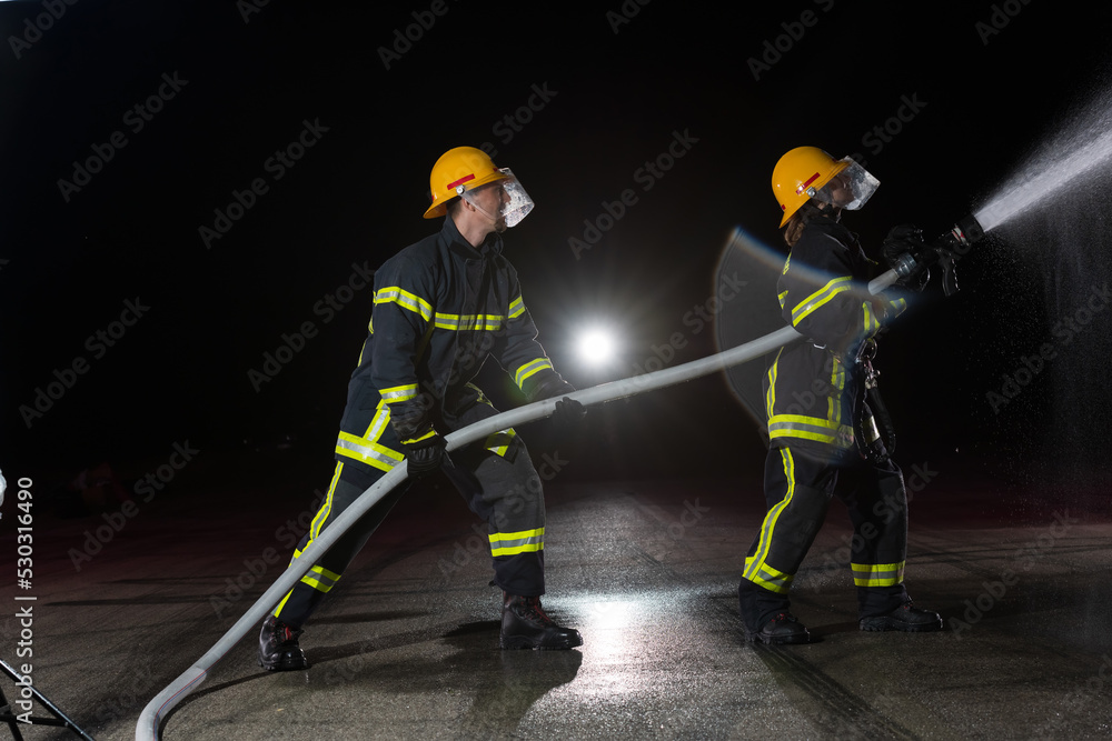 Obraz premium Firefighters using a water hose to eliminate a fire hazard. Team of female and male firemen in dangerous rescue mission. 