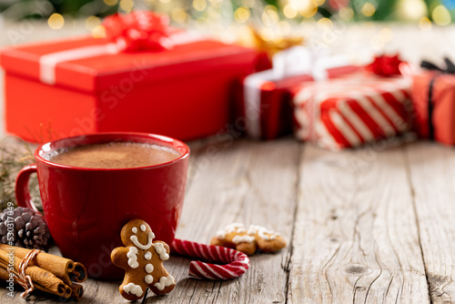 Image of gingerbread man, red cup, cinnamon sticks and christmas decoration on wood